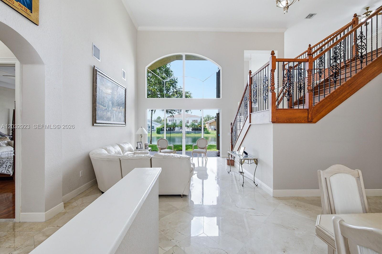 A bright living room features high ceilings, a grand staircase, and large windows overlooking water — 18543 SW 49th St, Miramar FL 33029, MIRAMAR, FL