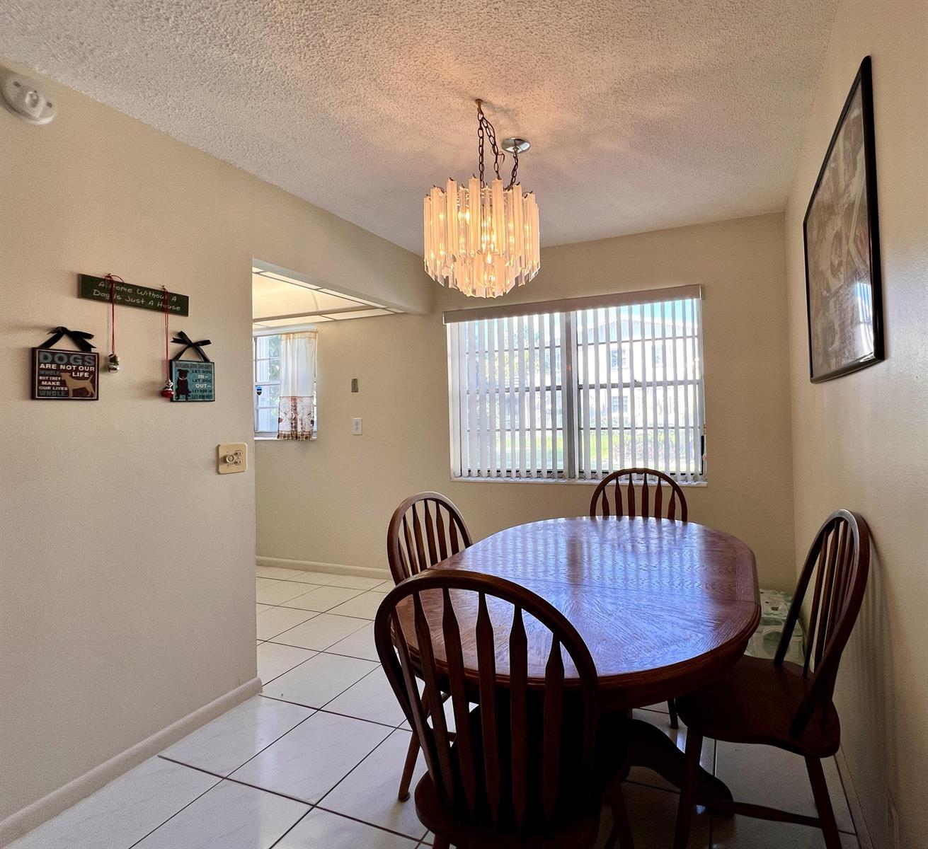 A dining area features a wooden table, four chairs, a crystal chandelier, and tile flooring — 76 Sheffield D, West Palm Beach FL 33417, WEST PALM BEACH, FL