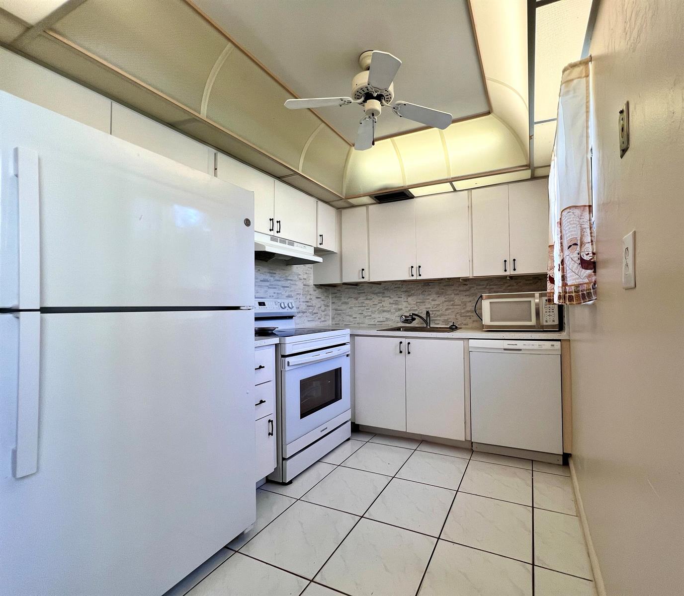 A kitchen features white appliances, white cabinetry, a tiled floor, and a ceiling fan — 76 Sheffield D, West Palm Beach FL 33417, WEST PALM BEACH, FL
