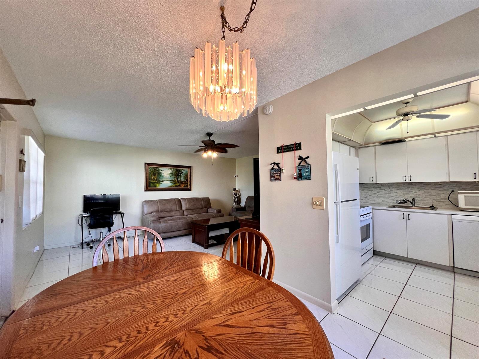 A dining area with a wood table overlooks a living room and a white kitchen — 76 Sheffield D, West Palm Beach FL 33417, WEST PALM BEACH, FL