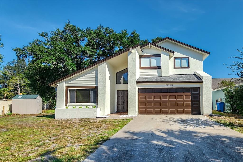 A two-story house with white stucco siding, a brown garage door, and a concrete driveway — 16169 GARDENDALE DRIVE, TAMPA, FL