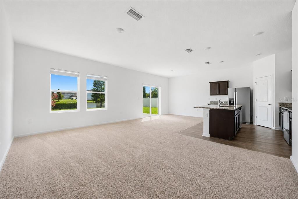 An open-concept living area features beige carpeting, a kitchen island, and sliding glass patio doors — 5506 TURKEY CREEK WAY, LAKELAND, FL