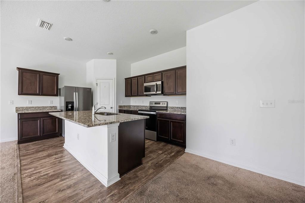 A kitchen features dark wood cabinets, granite countertops, a center island, and stainless steel appliances — 5506 TURKEY CREEK WAY, LAKELAND, FL