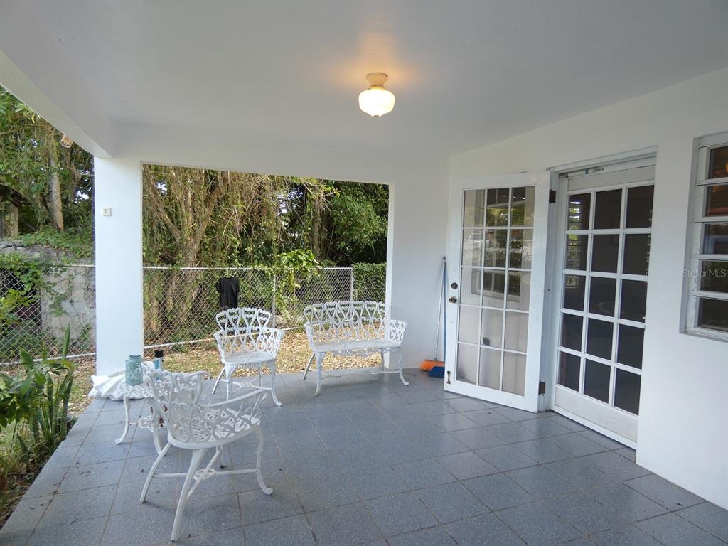 A covered patio features gray tiled flooring, white metal furniture, and glass-paned double doors — 37 CALLE CORAL, VIEQUES, PR