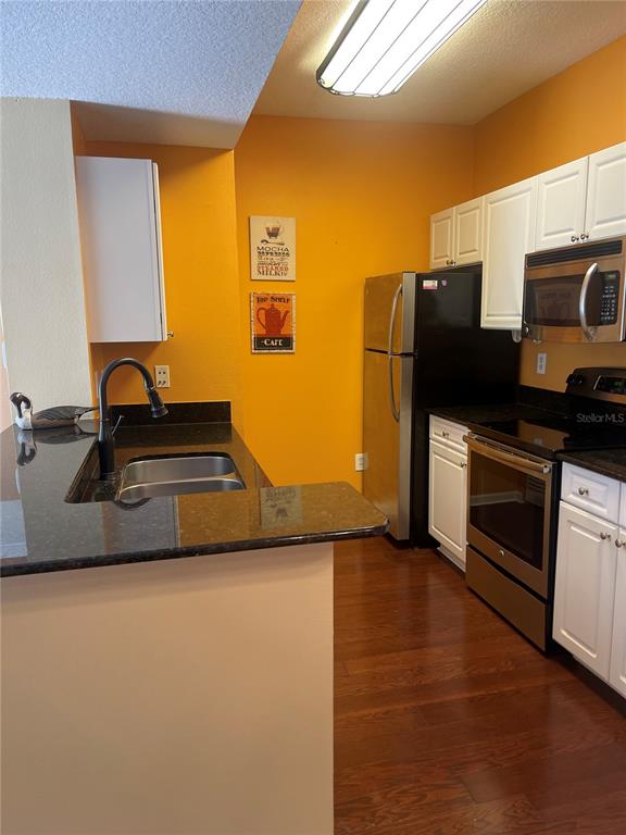 A kitchen features orange walls, white cabinets, dark countertops, and stainless steel appliances — 2001 TIZEWELL CIRCLE UNIT 1504, ORLANDO, FL