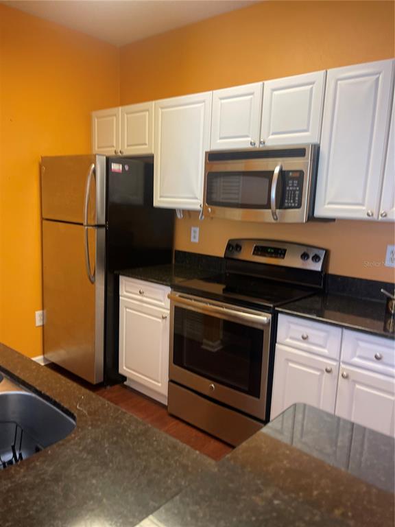 A kitchen features white cabinets, stainless steel appliances, and dark countertops against orange walls — 2001 TIZEWELL CIRCLE UNIT 1504, ORLANDO, FL
