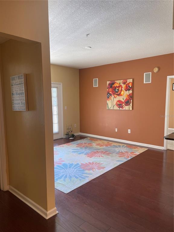 A room with dark wood flooring, a floral area rug, and a large poppy painting — 2001 TIZEWELL CIRCLE UNIT 1504, ORLANDO, FL