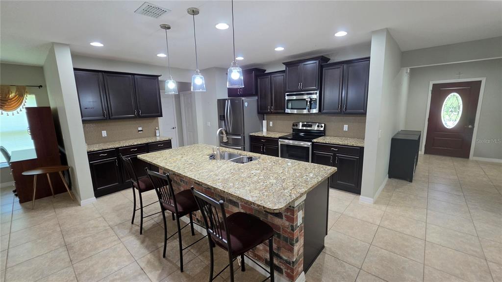 A kitchen features dark wood cabinets, granite countertops, a brick-faced island, and tile flooring — 3729 ISLES ARBOR LANE, KISSIMMEE, FL