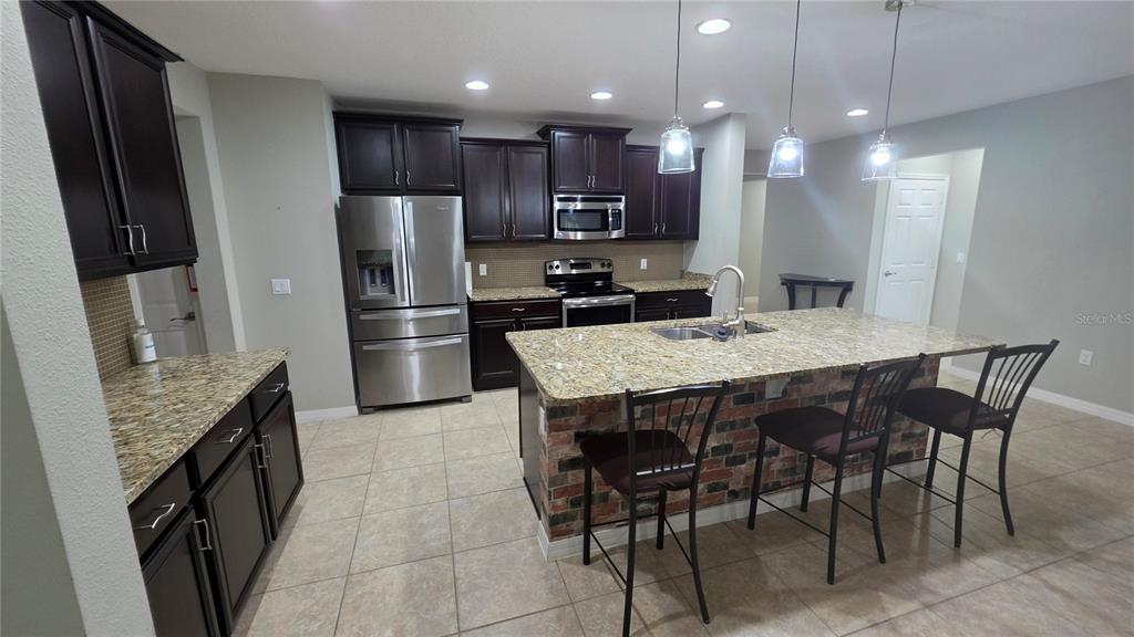 A kitchen features dark wood cabinets, granite countertops, a brick-faced island, and stainless steel appliances — 3729 ISLES ARBOR LANE, KISSIMMEE, FL