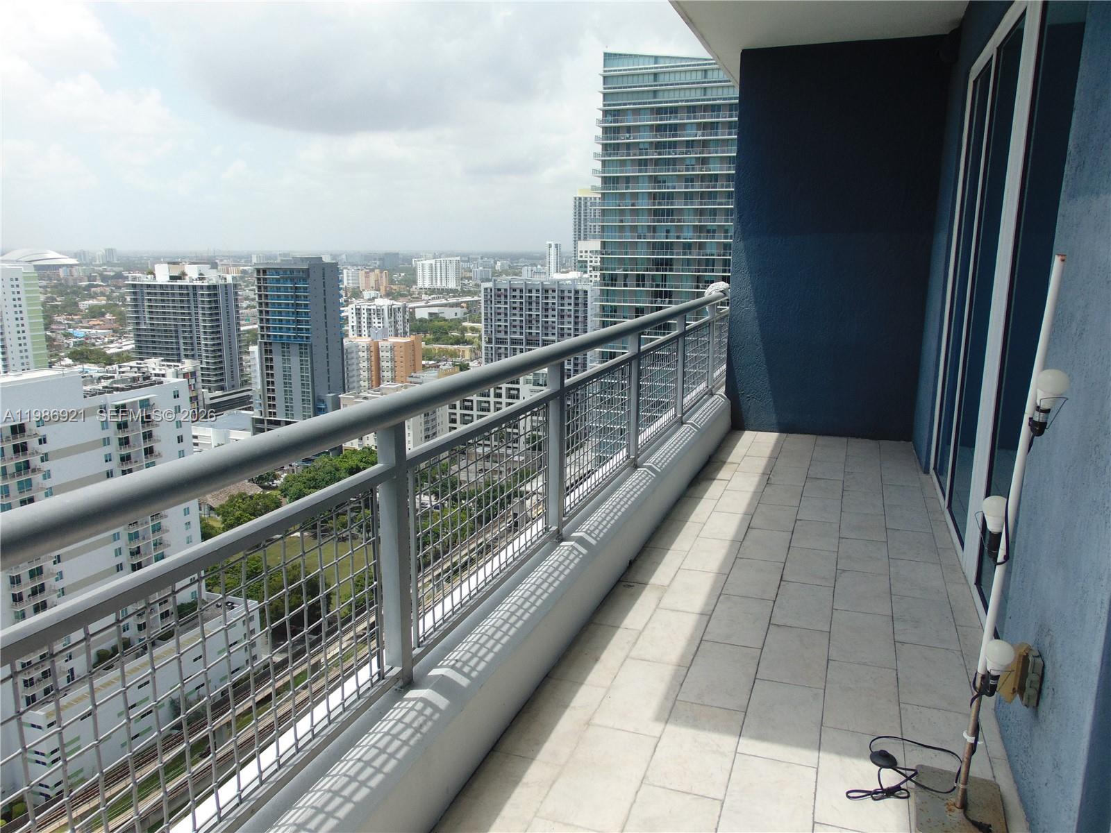 A high-rise balcony features tiled flooring, a metal railing, and a view of city buildings — 60 SW 13th St # 2619, Miami FL 33130, MIAMI, FL