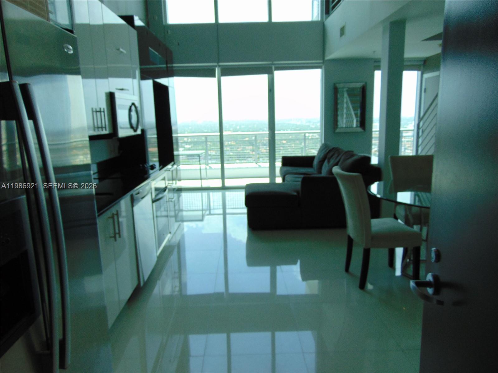 A modern kitchen with white cabinetry opens into a living area with floor-to-ceiling windows — 60 SW 13th St # 2619, Miami FL 33130, MIAMI, FL