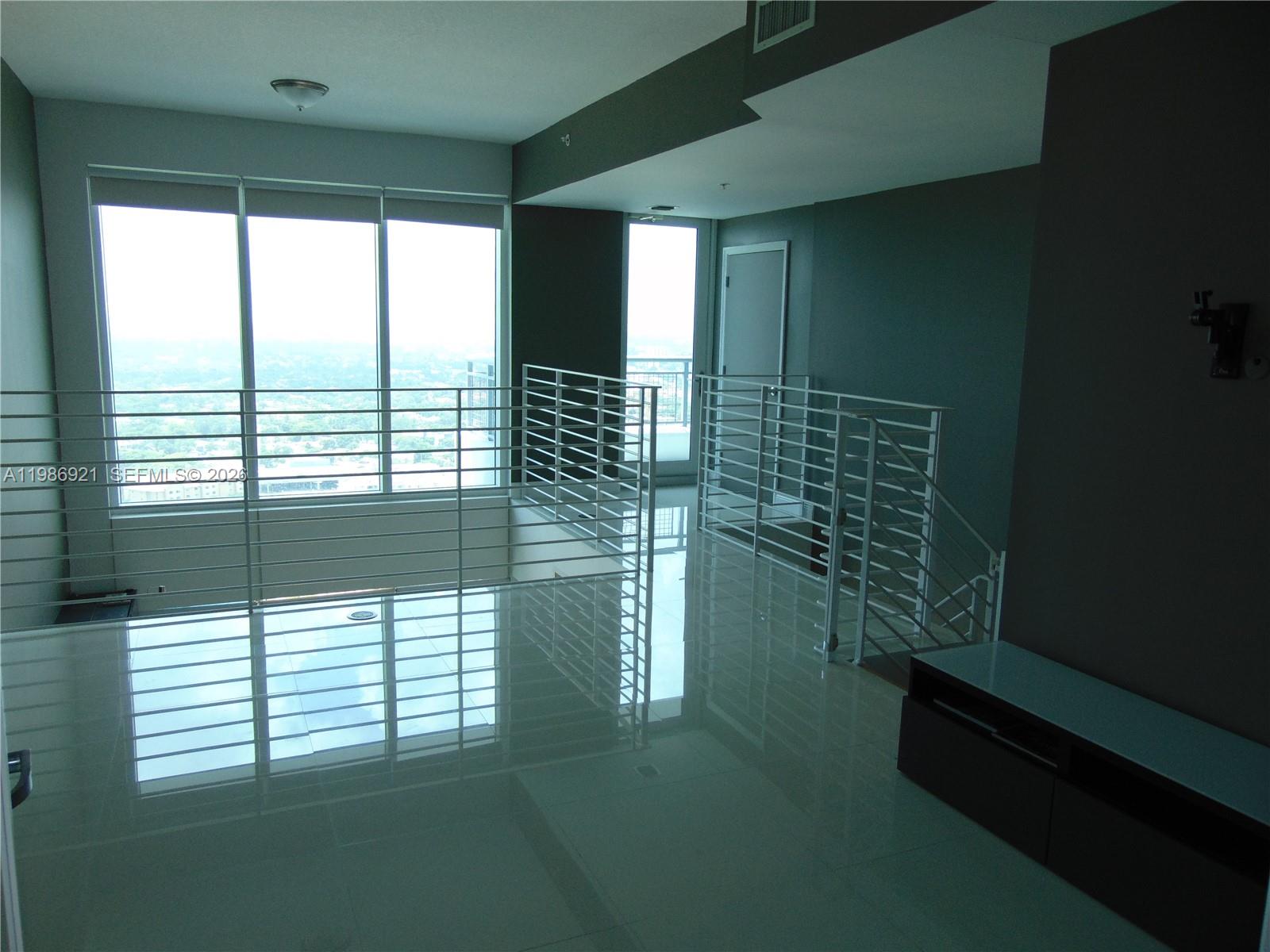 A modern loft space features white tile floors, metal railings, and large windows overlooking a city — 60 SW 13th St # 2619, Miami FL 33130, MIAMI, FL