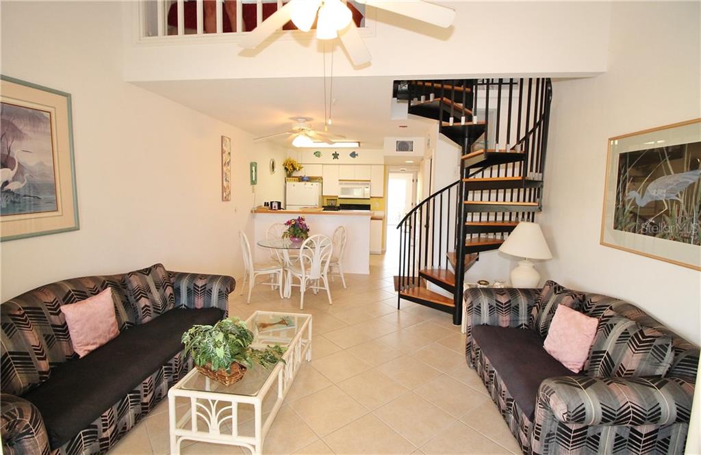 A living room with tile floors, two patterned sofas, a spiral staircase, and a dining area — 9400 LITTLE GASPARILLA ISLAND UNIT H8, PLACIDA, FL