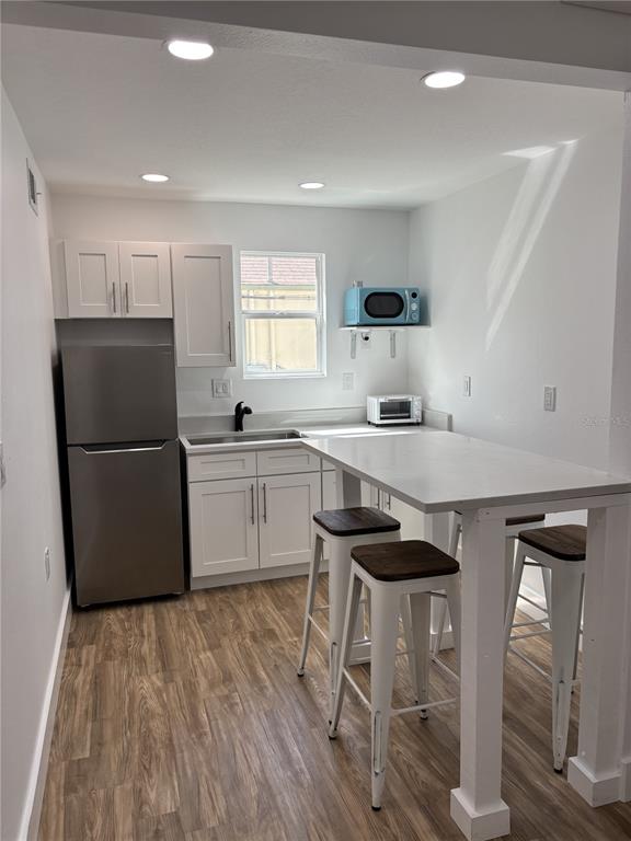 A small kitchen features white cabinets, stainless steel appliances, a breakfast bar, and wood-look flooring — 14141 GULF BOULEVARD UNIT 5, MADEIRA BEACH, FL