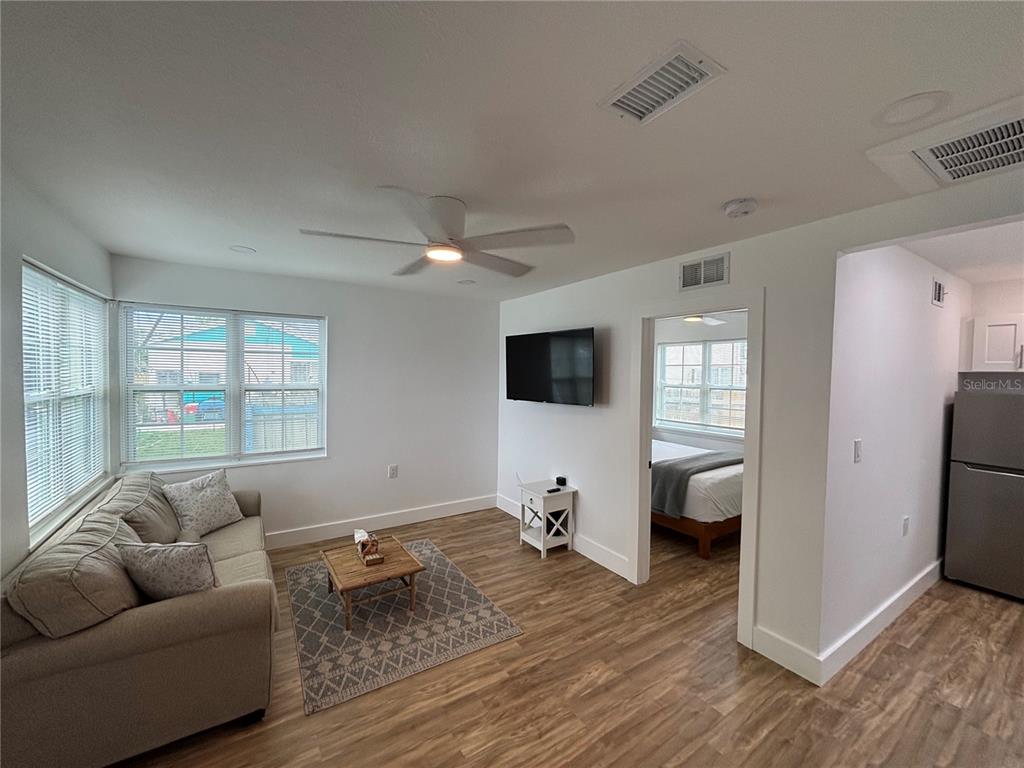 A living room with light wood flooring, a sofa, a television, and an adjacent bedroom — 14141 GULF BOULEVARD UNIT 5, MADEIRA BEACH, FL