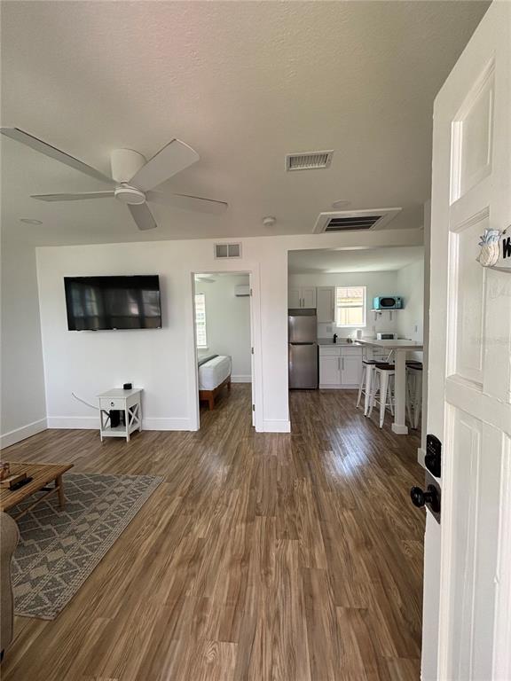 An open-concept living area with wood-look flooring leads to a kitchen and a bedroom — 14141 GULF BOULEVARD UNIT 5, MADEIRA BEACH, FL