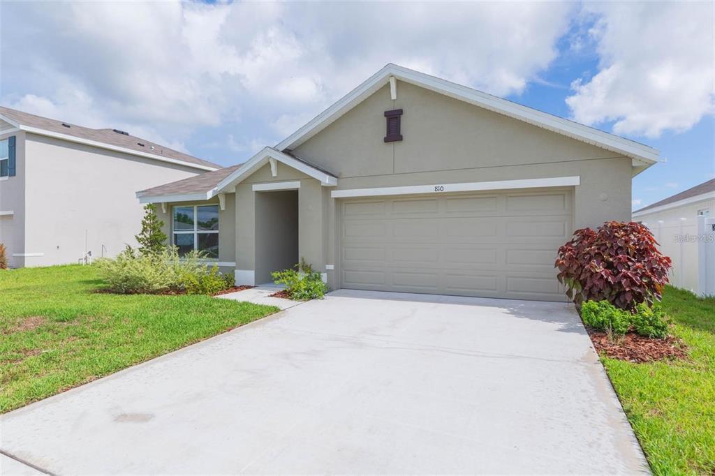 A single-story house with a beige stucco exterior, a two-car garage, and a concrete driveway — 810 ACE OUTLAW AVENUE, RUSKIN, FL
