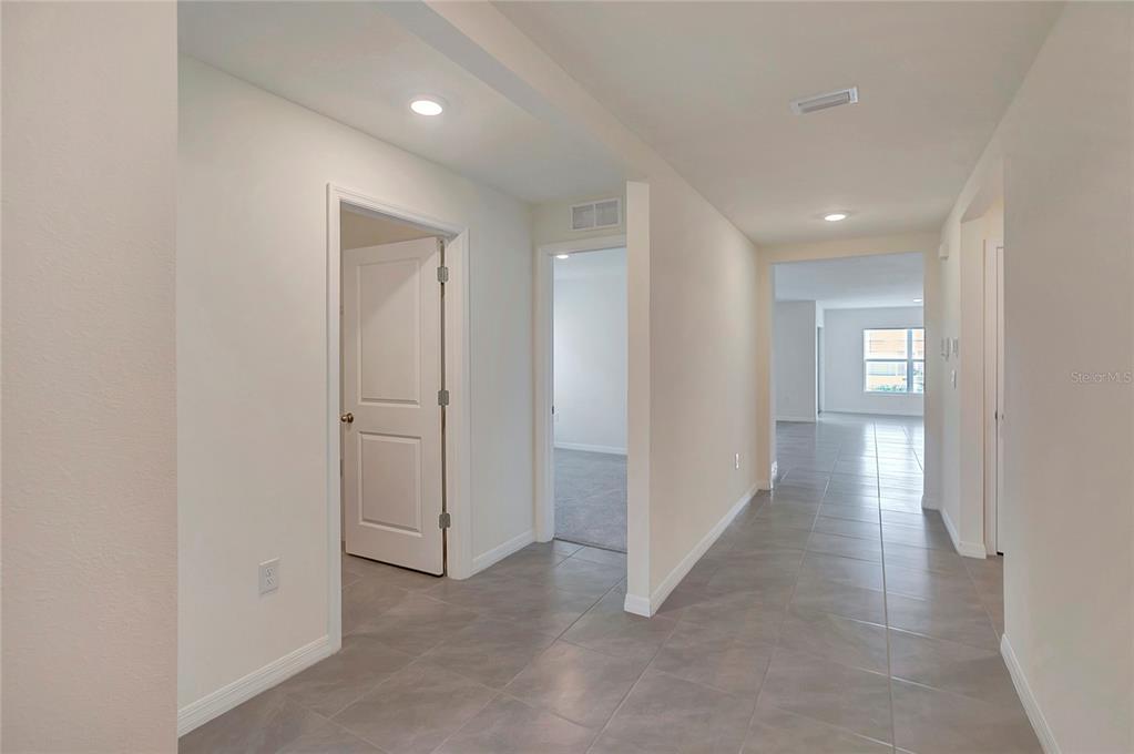 A hallway with gray tile flooring leads to an open living area and bedrooms — 810 ACE OUTLAW AVENUE, RUSKIN, FL