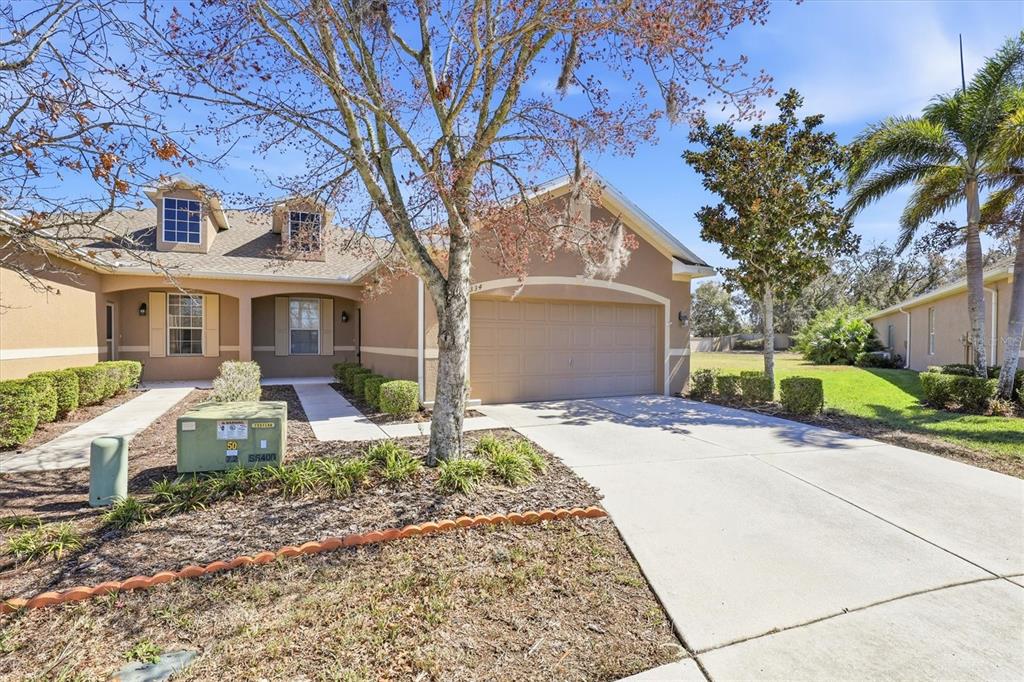 A tan single-story house with a two-car garage, a concrete driveway, and a front lawn — 2334 BARRACUDA COURT, HOLIDAY, FL