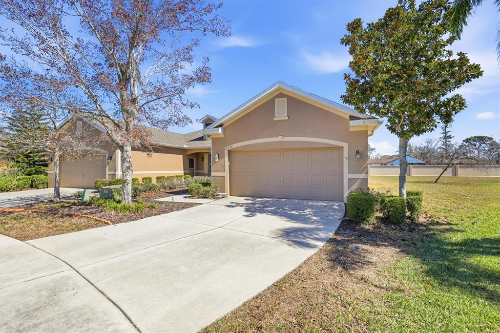 A tan single-story house features two garage doors, a concrete driveway, and surrounding trees — 2334 BARRACUDA COURT, HOLIDAY, FL