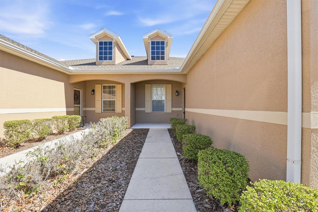 A concrete walkway leads to the recessed front entrance of a beige stucco house — 2334 BARRACUDA COURT, HOLIDAY, FL