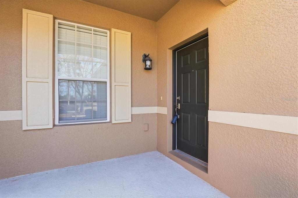 A tan stucco exterior features a dark front door and a window with shutters — 2334 BARRACUDA COURT, HOLIDAY, FL