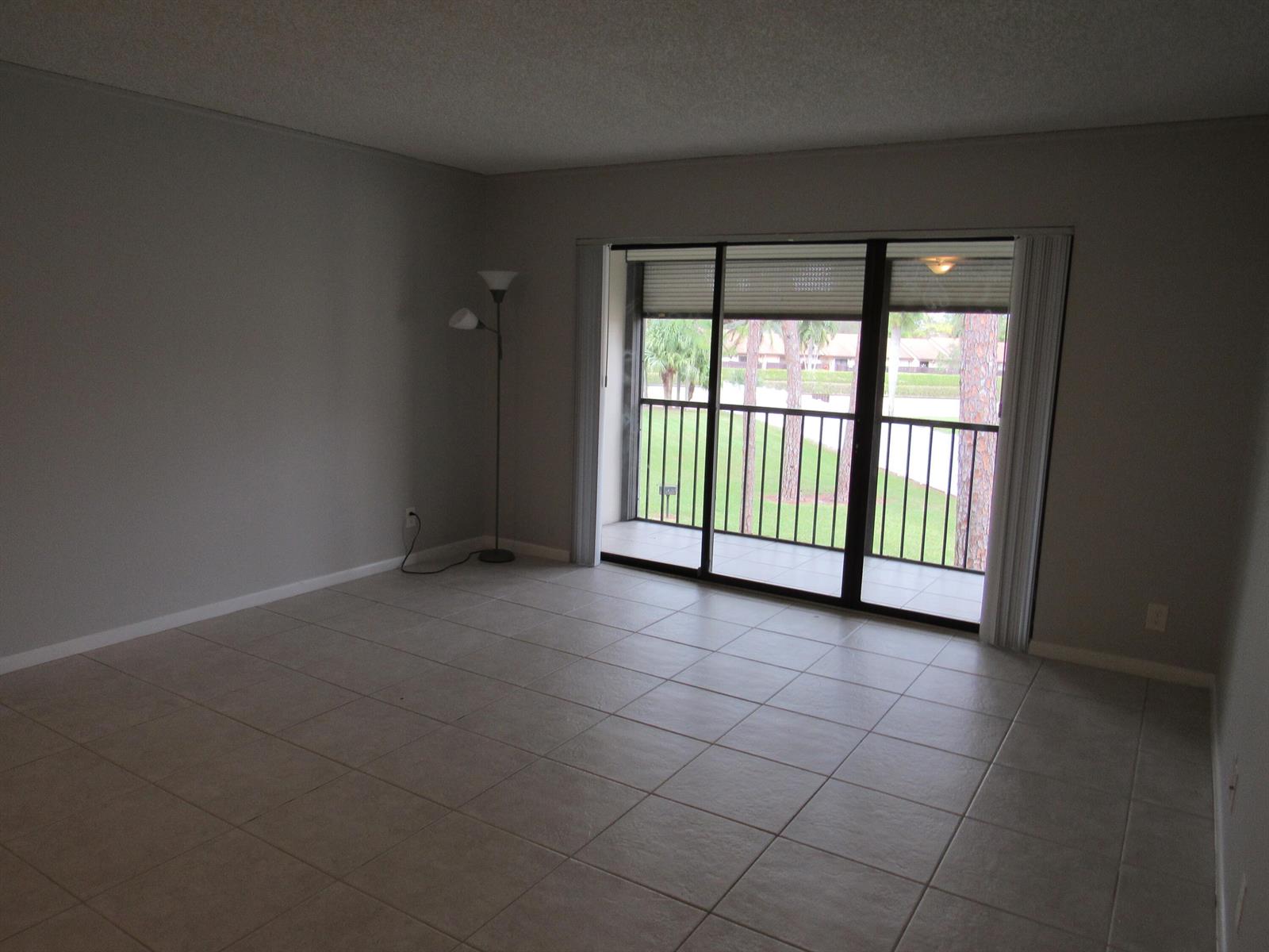 An empty living room with light tile flooring, gray walls, and a sliding glass balcony door — 703 Sunny Pine Way # G2, FL 33415, FL