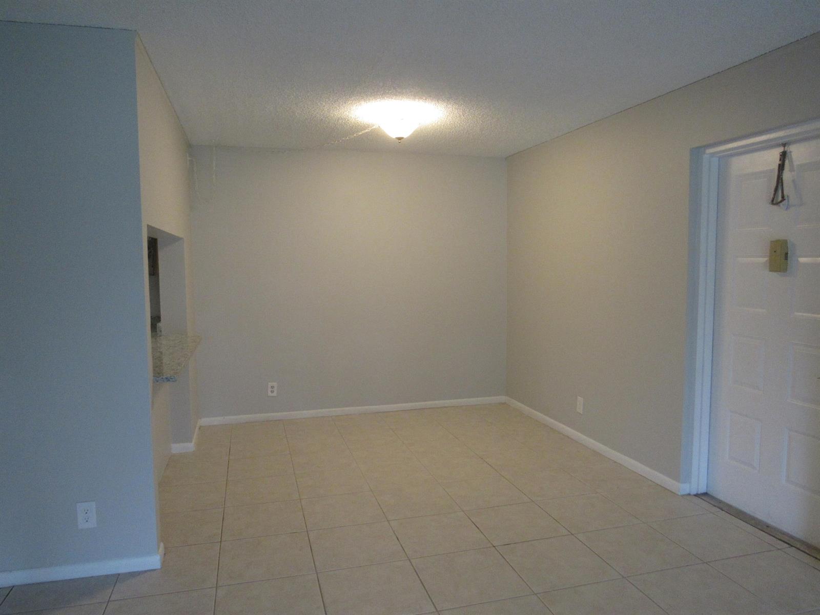 An empty room with light-colored tile flooring, gray walls, and a central ceiling light fixture — 703 Sunny Pine Way # G2, FL 33415, FL