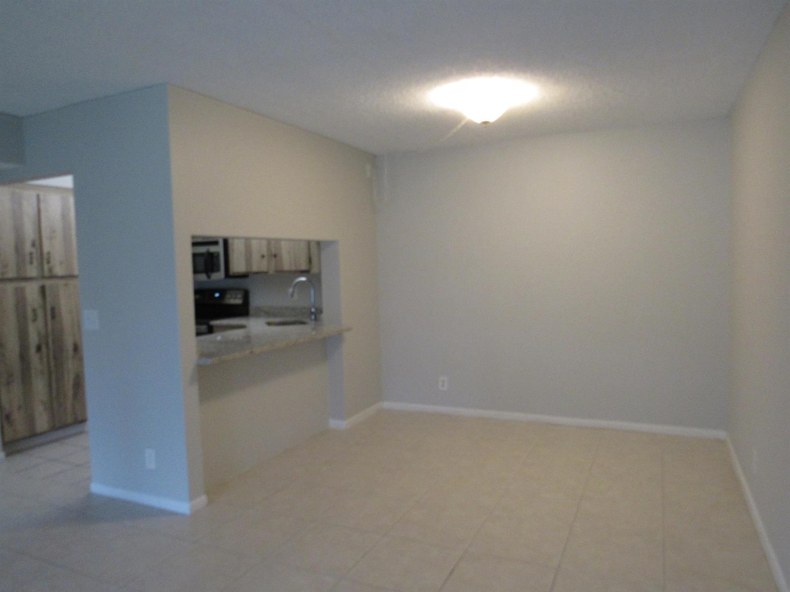 An open dining area features light-colored tile flooring and a pass-through window to the kitchen — 703 Sunny Pine Way # G2, FL 33415, FL