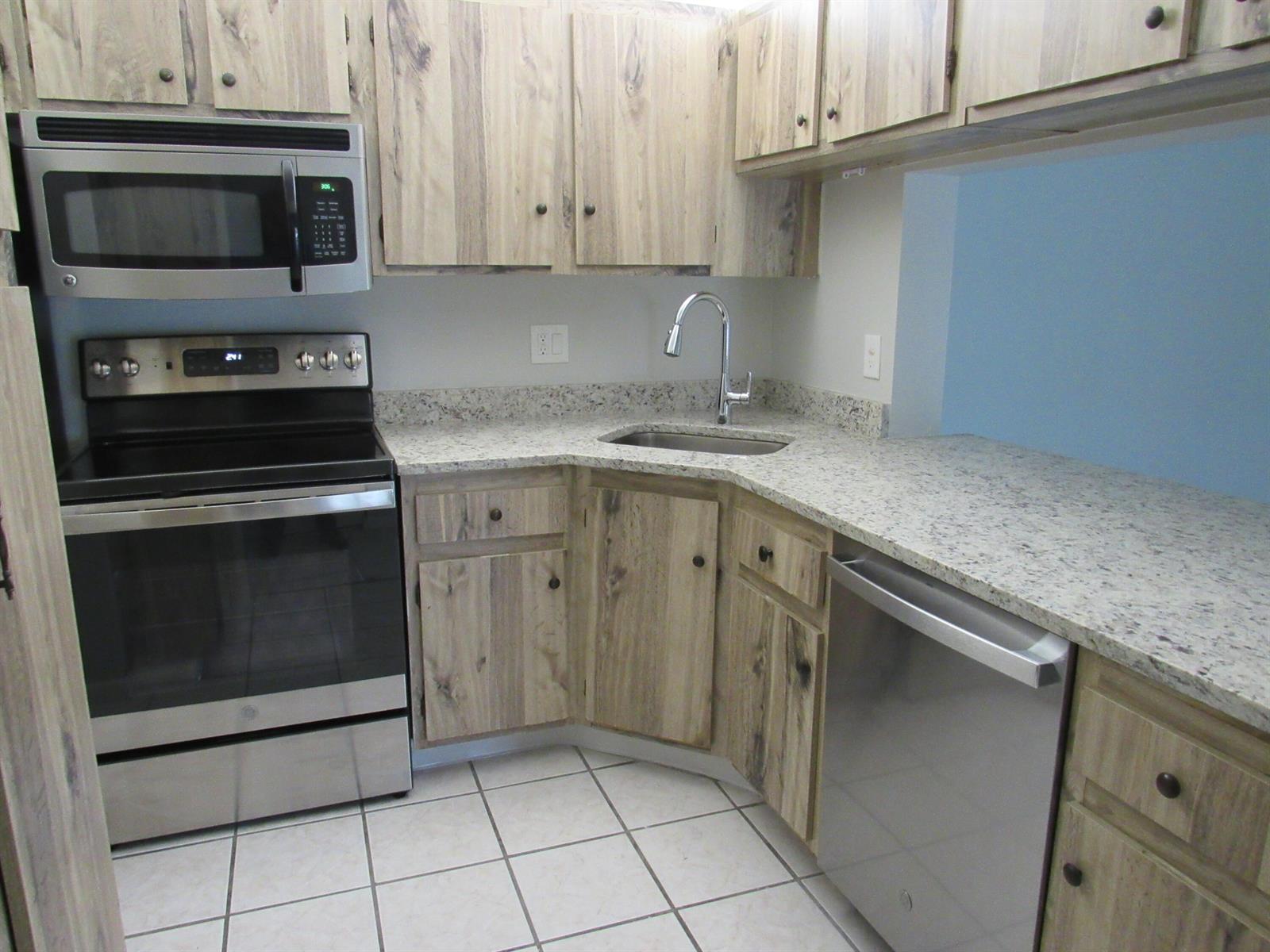 A kitchen features stainless steel appliances, wood-grain cabinets, and speckled granite countertops — 703 Sunny Pine Way # G2, FL 33415, FL