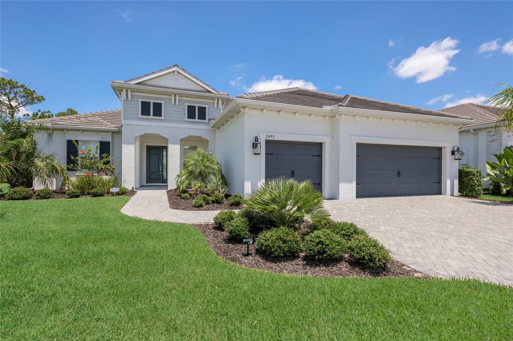 A single-story house with a white stucco exterior, gray garage doors, and a paved driveway — 2493 PARADISE PLUM DRIVE, SARASOTA, FL