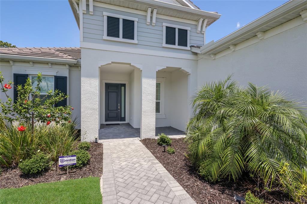 A paved walkway leads to the covered entryway of a house with light-colored exterior walls — 2493 PARADISE PLUM DRIVE, SARASOTA, FL