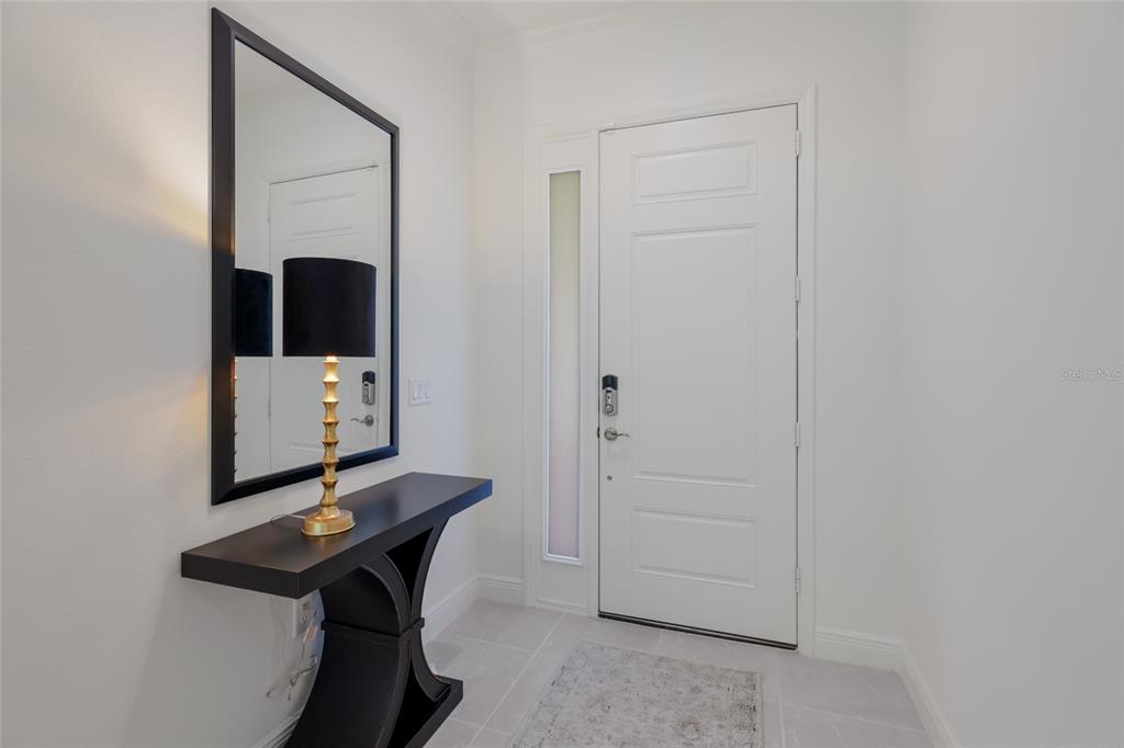 A modern entryway features a white door, a black console table, and a wall mirror — 2493 PARADISE PLUM DRIVE, SARASOTA, FL