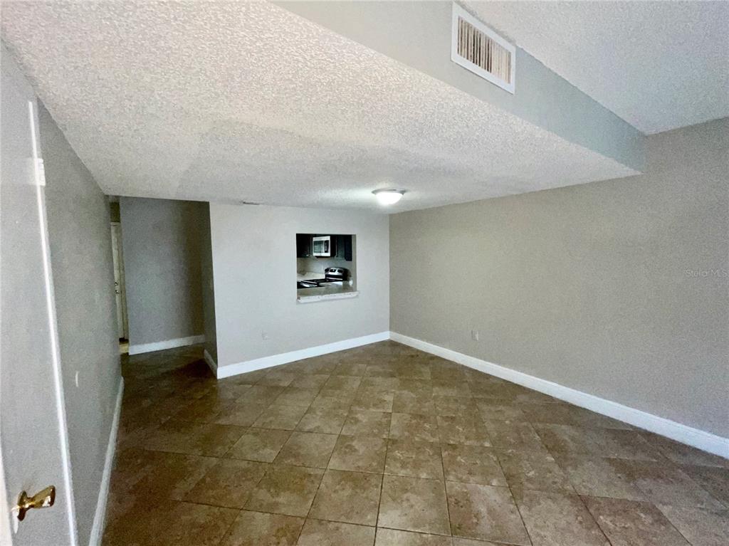 An empty room with tiled floors features a pass-through window looking into a kitchen — 4263 S SEMORAN BOULEVARD UNIT 9, ORLANDO, FL