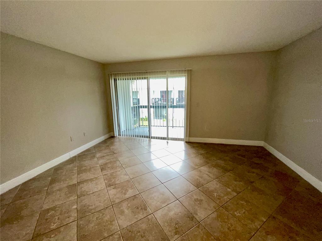 An empty room features beige walls, tile flooring, and a sliding glass door to a balcony — 4263 S SEMORAN BOULEVARD UNIT 9, ORLANDO, FL