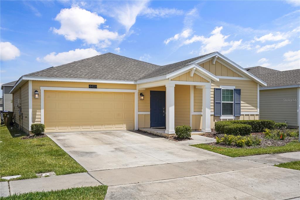 A yellow, single-story suburban house features a two-car garage and a covered front porch — 4409 BLACKBIRD STREET, KISSIMMEE, FL