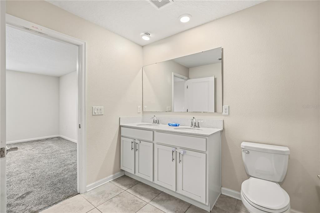 A bathroom features a double-sink vanity with white cabinets, a large mirror, and tiled flooring — 4409 BLACKBIRD STREET, KISSIMMEE, FL
