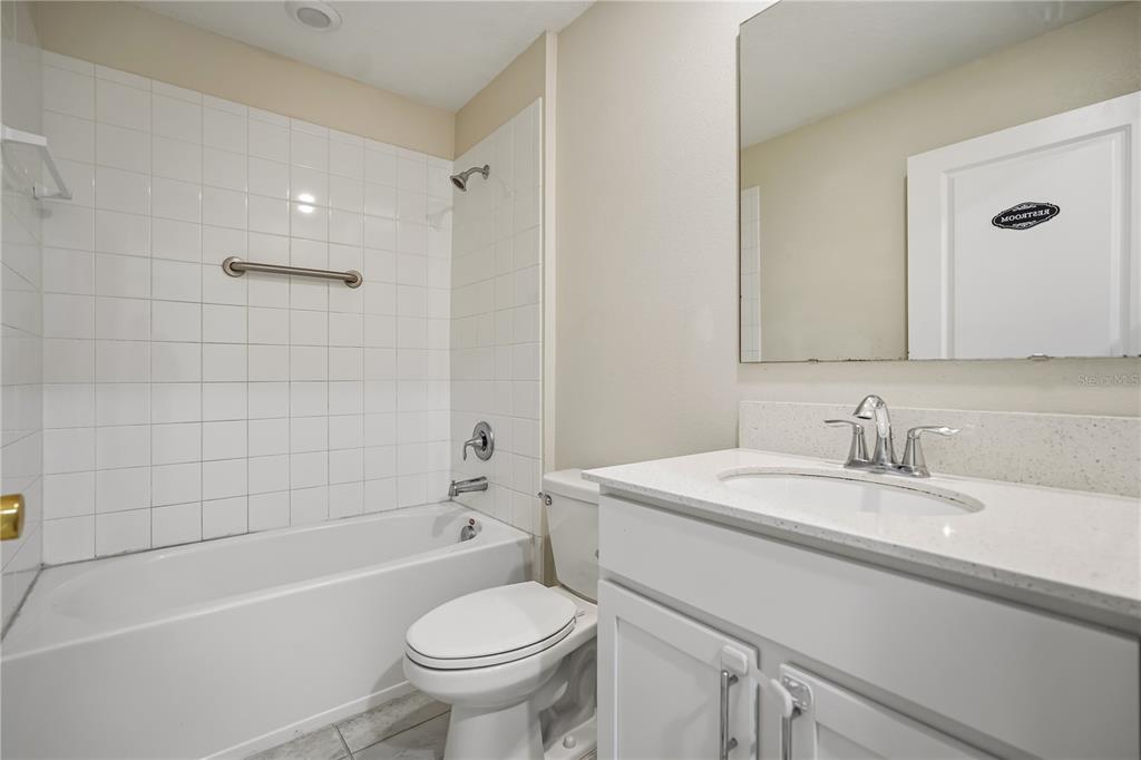 A bathroom features a white vanity, a toilet, and a shower-tub combo with white tiles — 4409 BLACKBIRD STREET, KISSIMMEE, FL