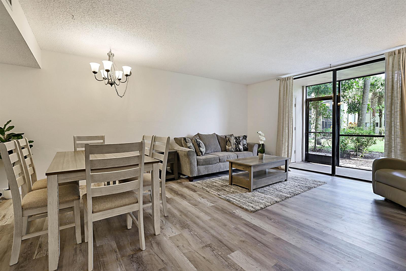 A living and dining area with wood-look flooring, a gray sofa, and a sliding glass door — 5160 Las Verdes Circle # 117, Delray Beach FL 33484, DELRAY BEACH, FL