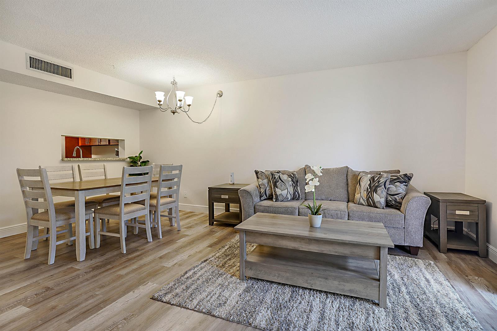 A living and dining area features light wood-look flooring, a gray sofa, and a chandelier — 5160 Las Verdes Circle # 117, Delray Beach FL 33484, DELRAY BEACH, FL