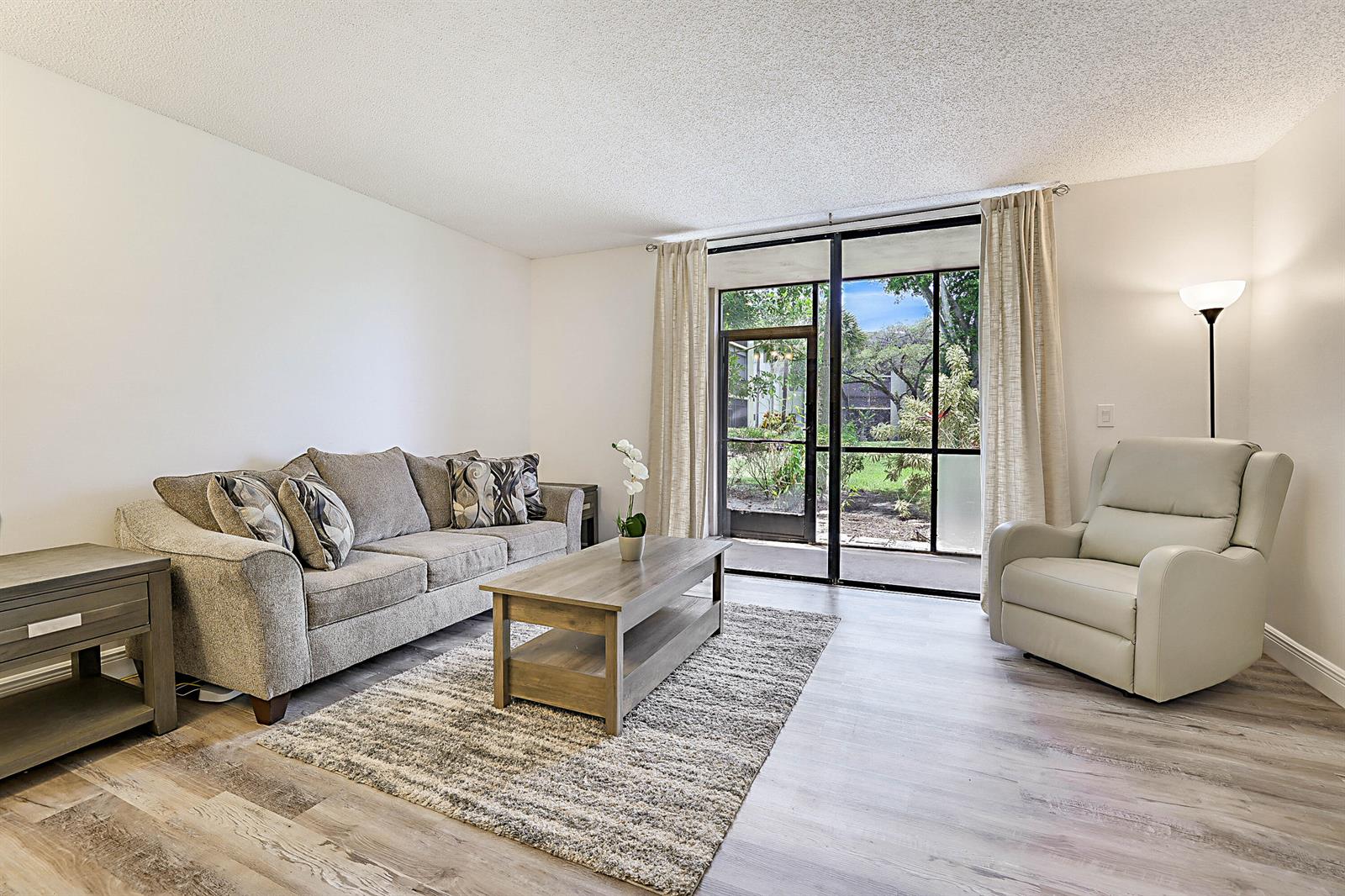 A living room features a gray sofa, a coffee table, a recliner, and a sliding door — 5160 Las Verdes Circle # 117, Delray Beach FL 33484, DELRAY BEACH, FL