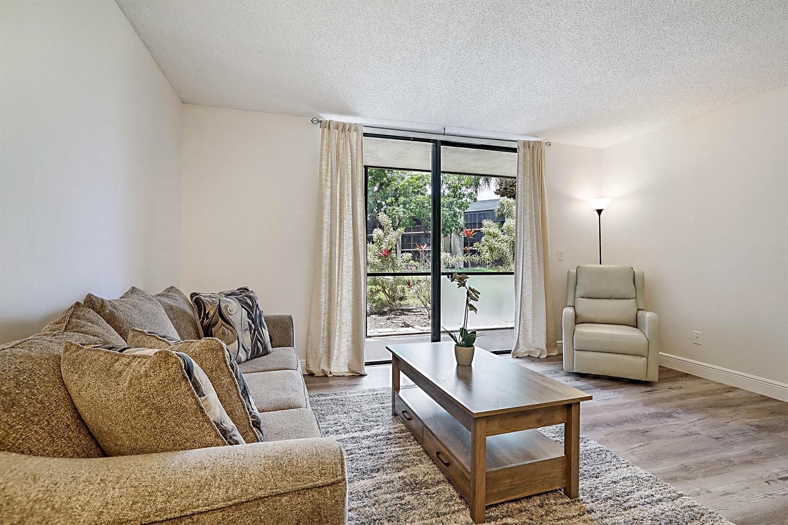 A living room features a beige sofa, wooden coffee table, armchair, and sliding glass doors — 5160 Las Verdes Circle # 117, Delray Beach FL 33484, DELRAY BEACH, FL