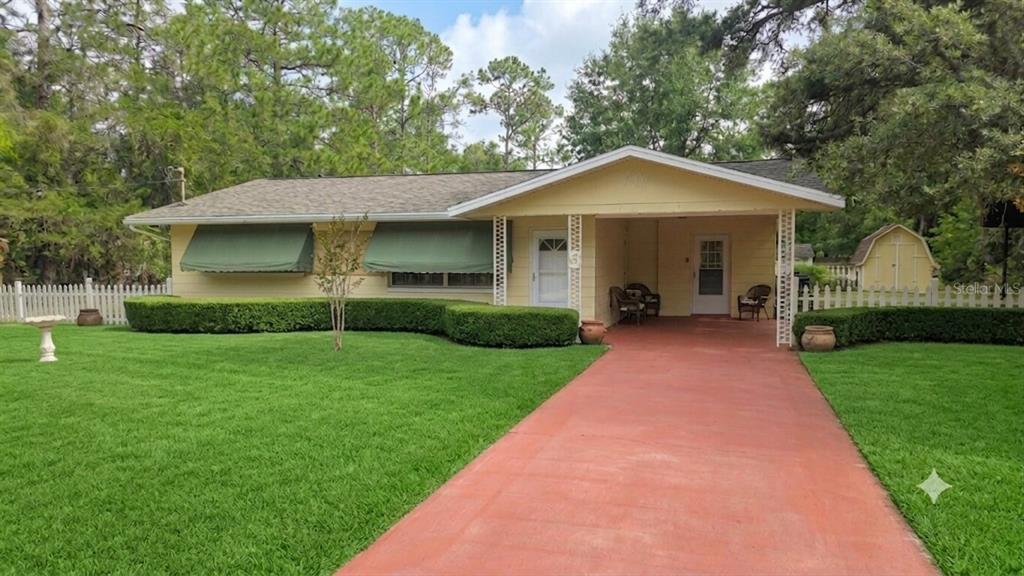 A yellow single-story house with a red driveway, green window awnings, and a white fence — 20851 SW AUDUBON AVENUE, DUNNELLON, FL