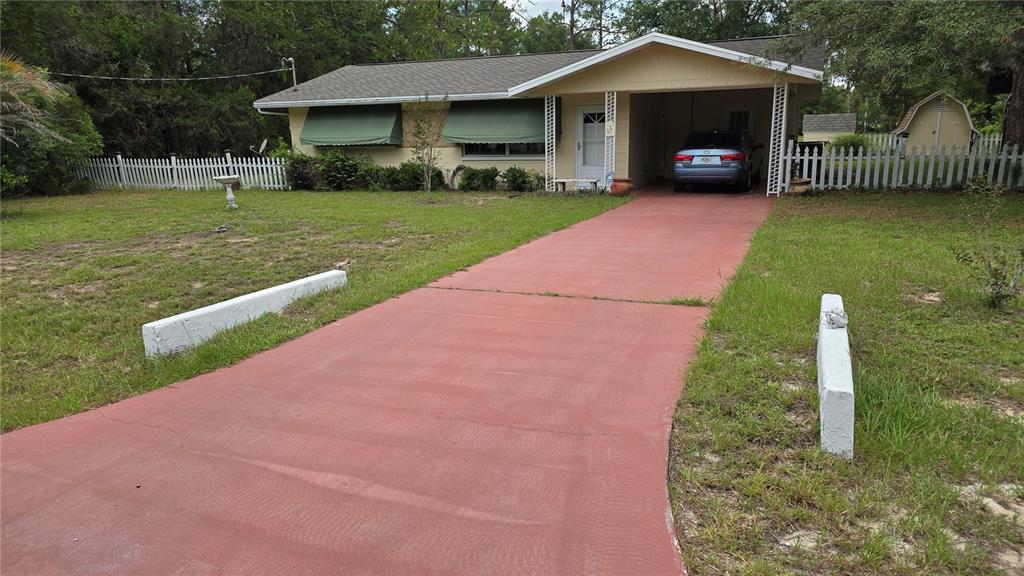 A single-story house with a red driveway, green window awnings, and a white picket fence — 20851 SW AUDUBON AVENUE, DUNNELLON, FL