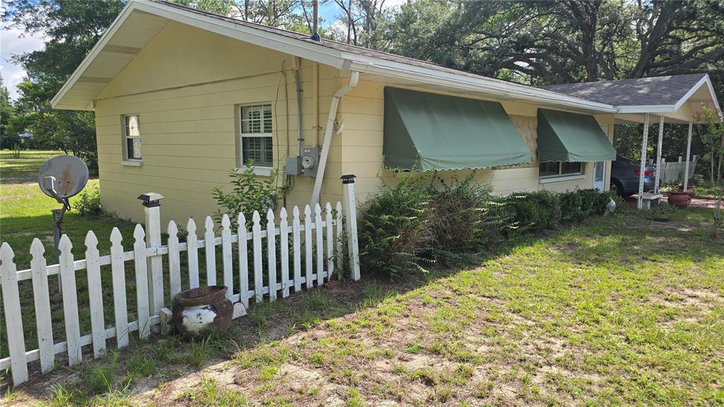 A yellow house with green awnings, a white picket fence, and a carport — 20851 SW AUDUBON AVENUE, DUNNELLON, FL