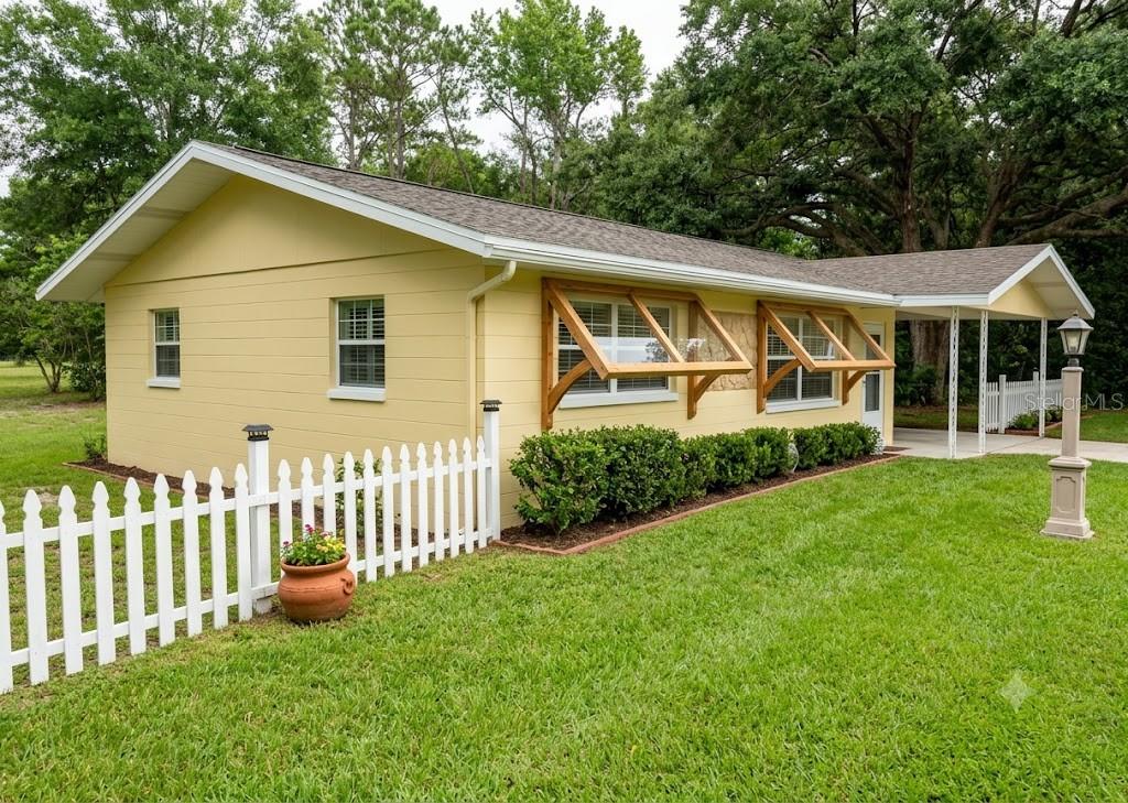 A yellow house with a white picket fence, wooden window awnings, and a carport — 20851 SW AUDUBON AVENUE, DUNNELLON, FL
