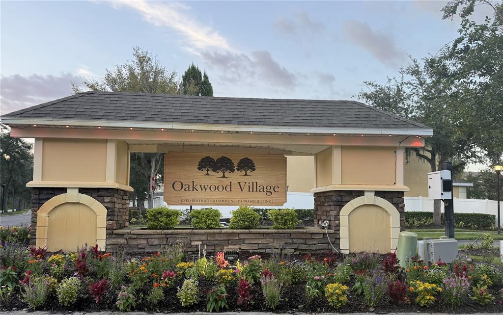A stone and stucco entrance sign for Oakwood Village sits behind a colorful flower bed — 8548 GABLEBEND WAY, TAMPA, FL