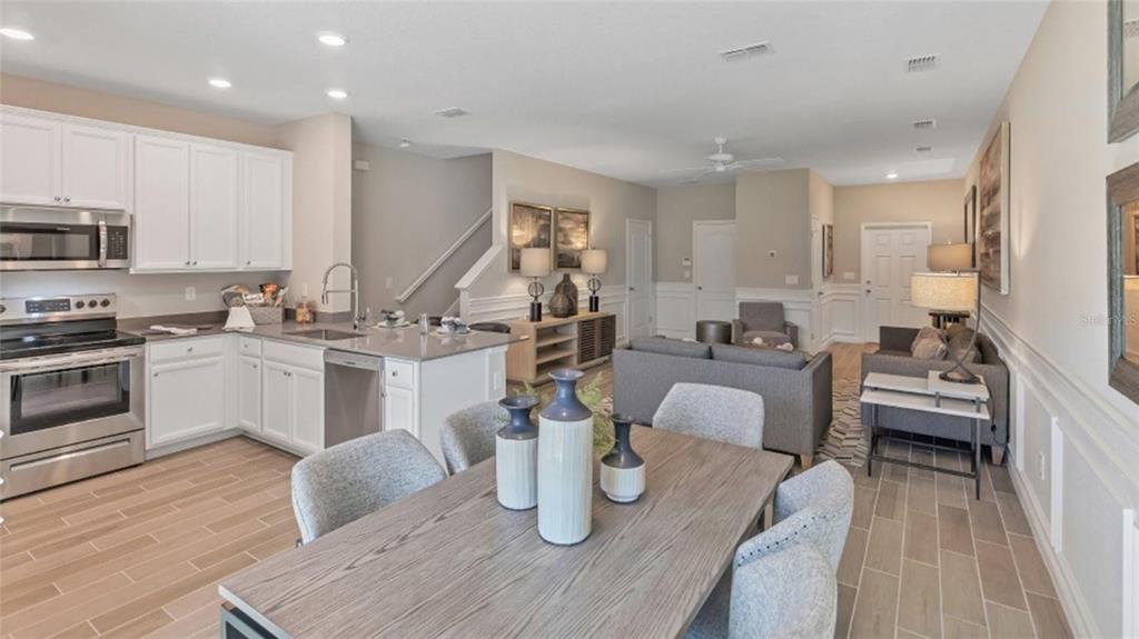 An open-concept kitchen, dining area, and living room featuring white cabinets and wood-look tile flooring — 3488 SE 37TH AVENUE ROAD, OCALA, FL