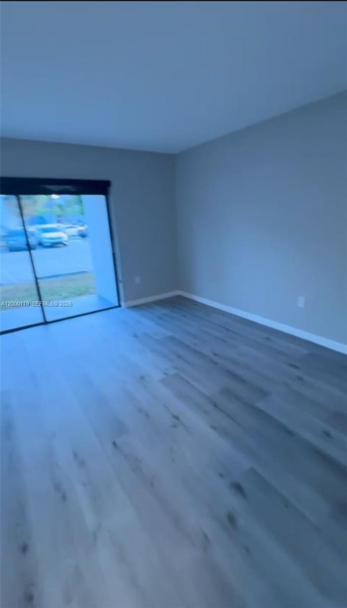 An empty room features light-colored wood-look flooring and a sliding glass door — 7100 NW 179th St # 102, Hialeah FL 33015, HIALEAH, FL