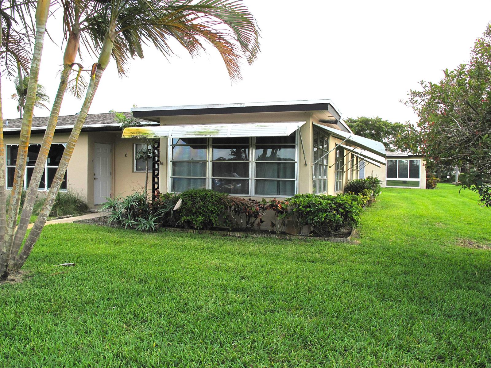 A single-story building with a flat roof, metal awnings, and palm trees in the yard — 892 N High Point Boulevard N # D, Delray Beach FL 33445, DELRAY BEACH, FL